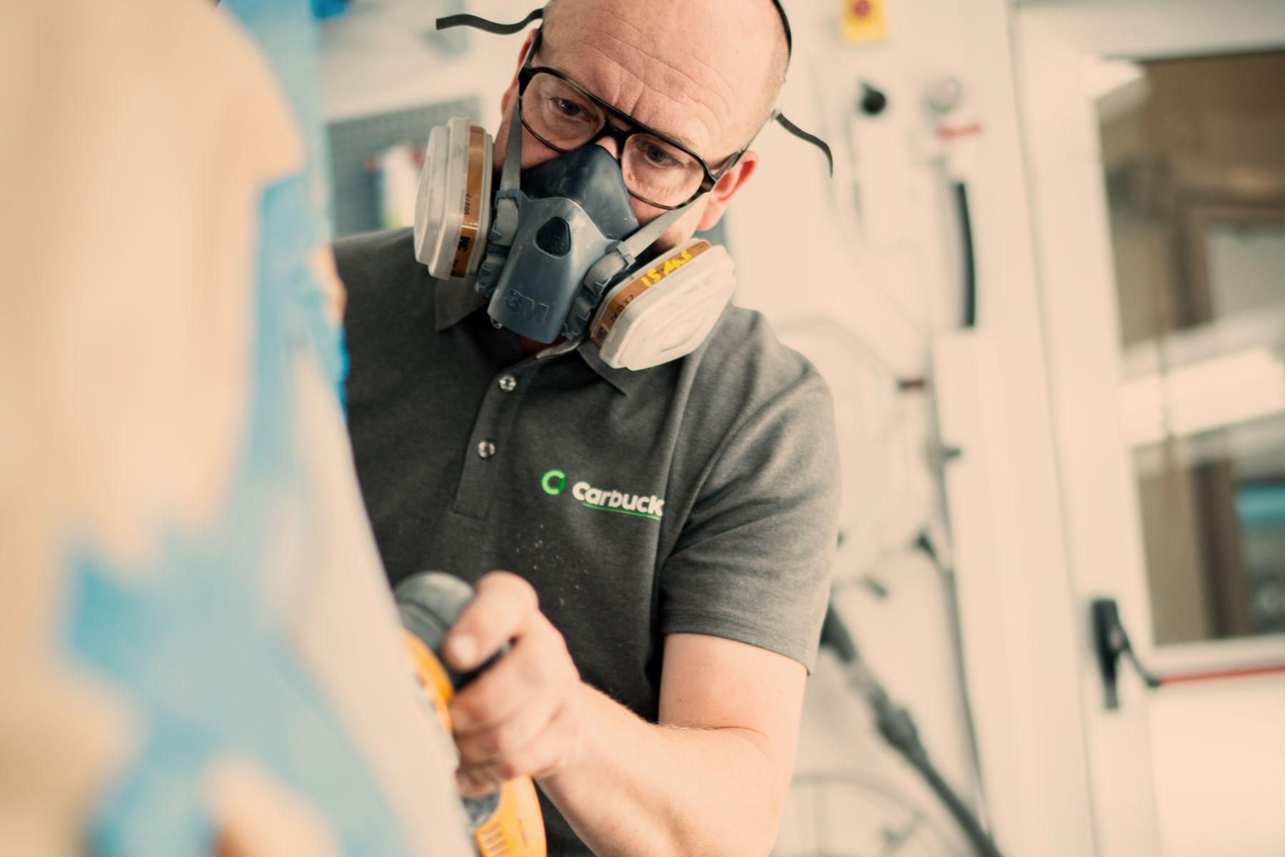 Tekniker fra Carbucks udfører slibning af bil før lakreparation med beskyttelsesudstyr